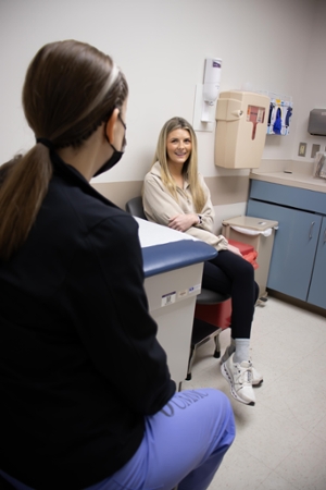 A patient smiling while sitting in clinic chair, talking with surgeon.